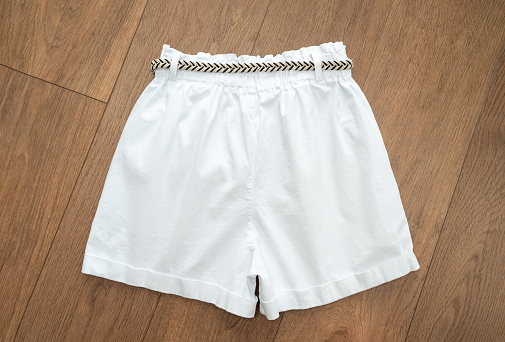 White denim shorts with a striped braided belt on a wooden background. Rear view, top view.