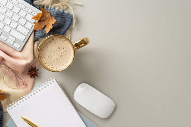istock Autumn-themed workplace at home. Top view image of keyboard and mouse, notepad, pen, mug of coffee, cashmere scarf, autumnal decorations with space for promotion on grey isolated background 1554257672
