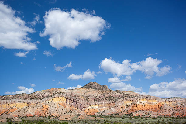 southwest badlands landscape orange and yellow badlands rise into the cloud filled blue sky with a smattering of green growth below.  such beautiful nature scenery can be found in the land of georgia o' keefe at ghost ranch, abiquiu new mexico.  horizontal composition. sonoran desert desert badlands mesa stock pictures, royalty-free photos & images