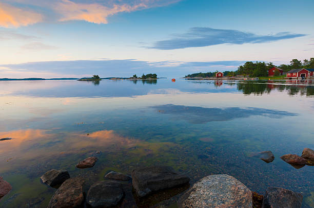 Sunset in the archipelago Sunset in the Swedish archipelago. A small boat passes in the distance. A typical red cottage is mirrored in the calm water. archipelago stock pictures, royalty-free photos & images