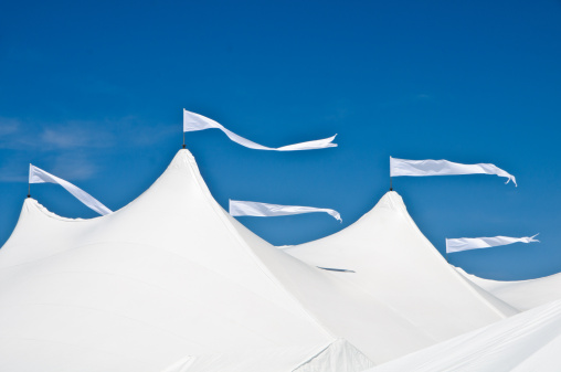 White pennants flutter in a stiff breeze atop a white wedding tent set up for a seaside reception on Cape Cod.