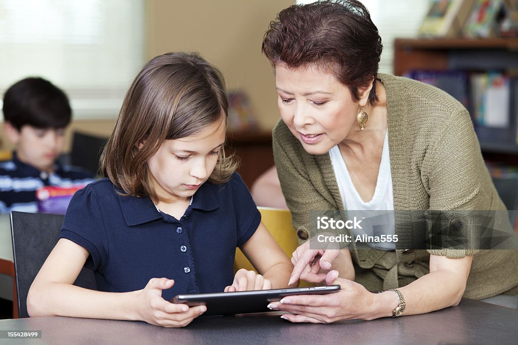 Insegnante aiutando gli studenti elementari su digital tablet con progetto - Foto stock royalty-free di 8-9 anni