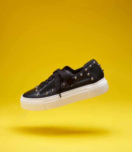 istock Modern black leather sneaker with textile insert, silver rivets and chunky white stitched sole flying on a bright yellow background with copy space. Levitation concept, lifestyle product photo. 1554285205