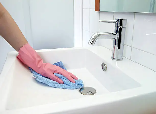 The woman, who is cleaning the washbasin with microfiber cloth and gloves
