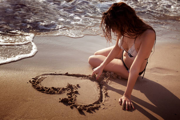 istock women at the beach drawing a heart 155428987
