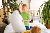 The red-haired girl is standing on the bed with a pillow in her hands. The kids had a pillow fight.