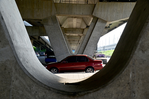 BANGKOK, THAILAND - August 4, 2023 : A red car is parked The space between the poles under the bridge highway, Thailand.