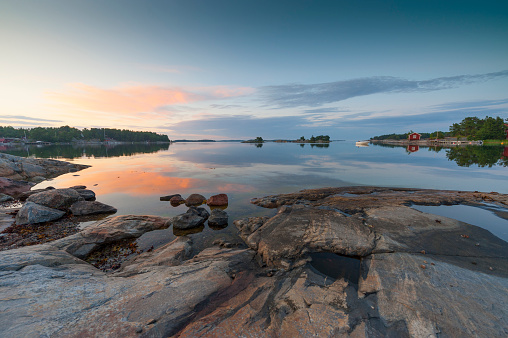 Sunset in the Swedish archipelago. A motor boat passes in the distance. A typical red cottage is mirrored in the calm water.