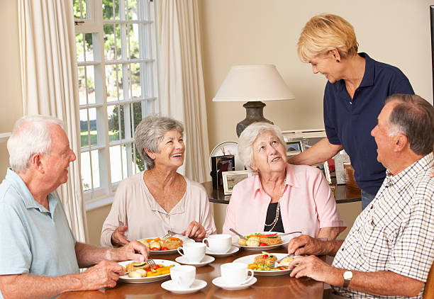 グループの高齢者のカップルのお食事と一緒にお楽しみいただけるようお手伝いいたします。 - senior adult nursing home eating home interior ストックフォトと画像