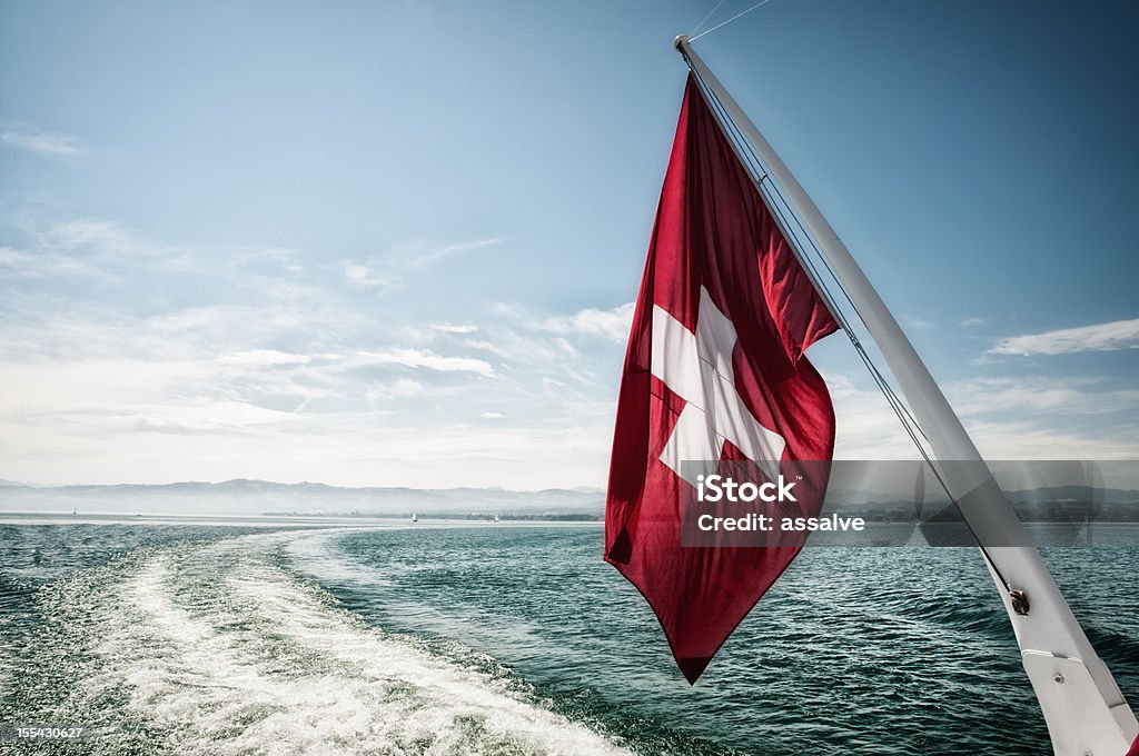 Swiss flag waving in the wind during a sailing boat trip on the Lake Constance in Switzerland, the lens flares are intended and added in afterprocess Swiss Flag Stock Photo