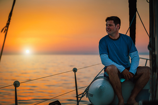 Man enjoying sailing on sailboat at sunset.