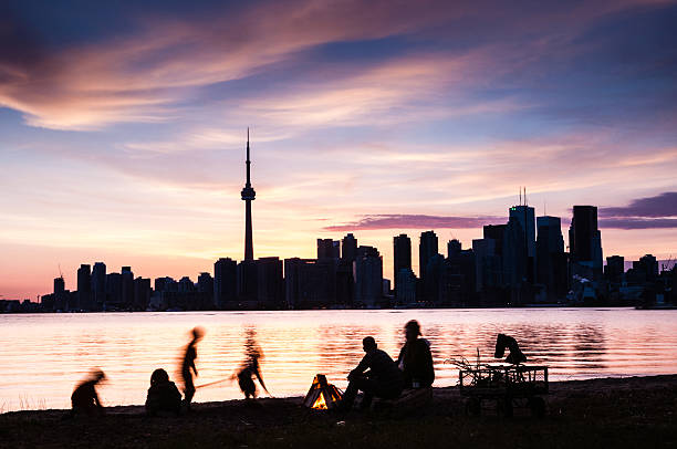 Family picnic at the shore of Toronto island with Toronto skyline at dusk on the background. Ontario. Canada.