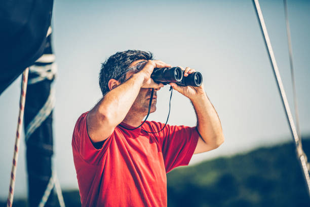 Sailor with binoculars on sailboat observing.