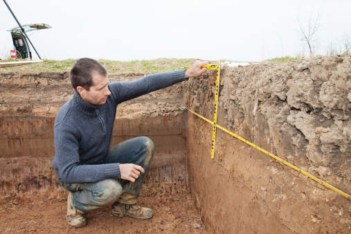 Male archaeologist using foot measure while working at an excavation site. Horizontal shot.