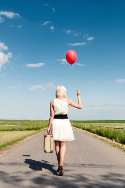 istock Woman walks away while holding balloon and suitcase 155431826