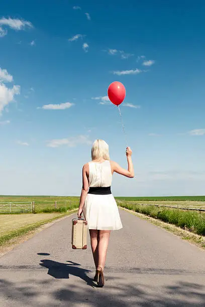 Photo of Woman walks away while holding balloon and suitcase