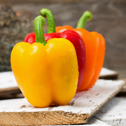 Yellow, red and orange bell peppers in a row on an old wood board.