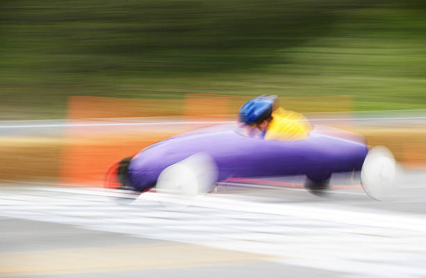 Soapbox Derby Race Car Child Soap box derby car crosses the finish line in abstract motion blur.  The Soap Box Derby is a youth car racing program which has been run in the United States since 1934. World Championship finals are held each July at Derby Downs in Akron, Ohio. Race cars are unpowered, relying entirely upon gravity to move downhill.  Early cars were constructed of wood from crates and other scrap sources, with wheels from baby buggies and wagons.  Today, using standardized wheels with precision ball bearings, modern racers start on a ramp at the top of a hill, and attain speeds of up to 35 miles per hour.  Irondequoit, New York, 2008. soapbox cart stock pictures, royalty-free photos & images