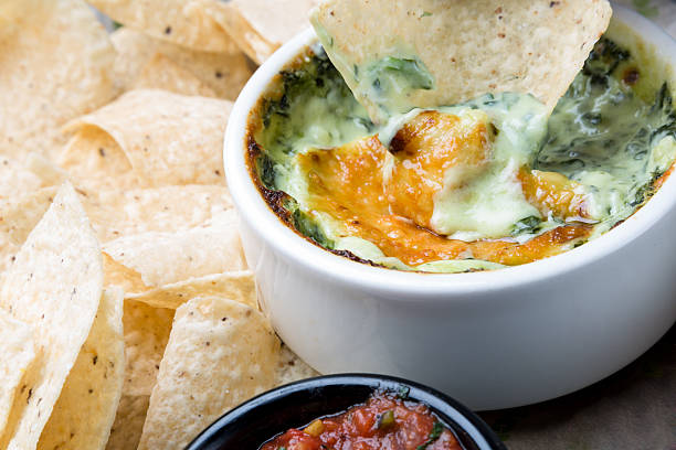 Cheesy Spinach Dip Tortilla chip dipping into Cheesy Spinach Dip artichoke stock pictures, royalty-free photos & images