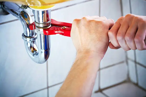 Photo of Plumber hands holding wrench and fixing a sink in bathroom