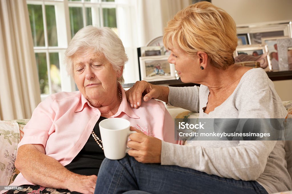 Adulte fille visitant malheureux Senior mère assise sur un canapé-lit - Photo de Fille de libre de droits