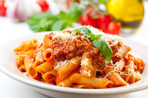 Bolognese pens Plate of penne bolognese with ingredients in the background. bolognese sauce stock pictures, royalty-free photos & images