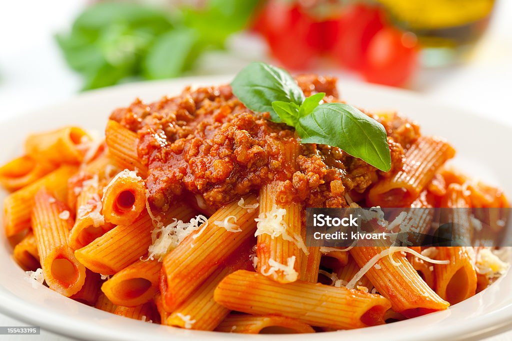 Close-up of the orange-toned penne Bolognese Plate of penne bolognese with ingredients in the background. Bolognese Sauce Stock Photo