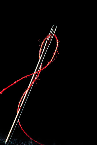 Needle and red thread on dark background. Lot of copy space