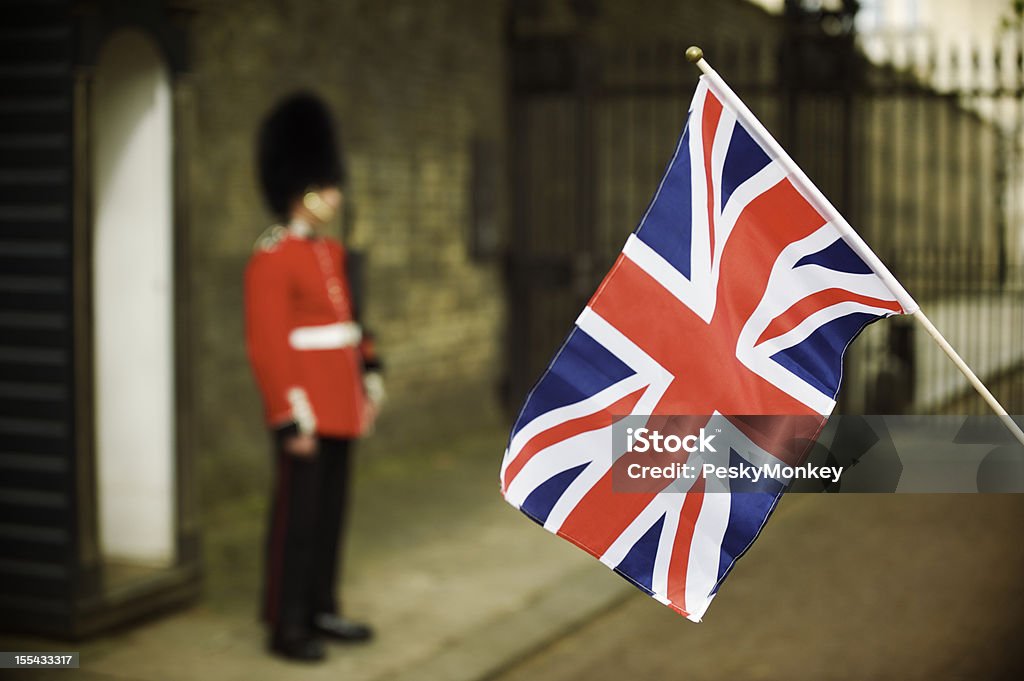 Union Jack Flag Waves Next to Soldier in Red Union Jack flag waves next to a guard in bright red uniform Honor Guard Stock Photo