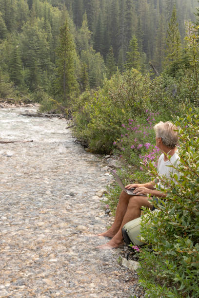 istock Senior man uses digital tablet while resting by creek edge 1554355699