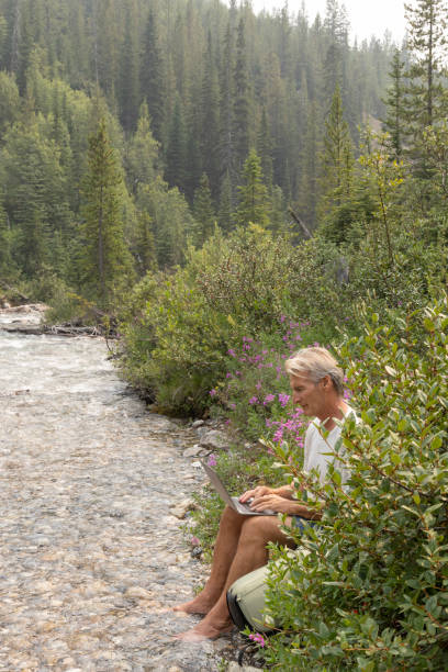 istock Senior man uses digital tablet while resting by creek edge 1554355700