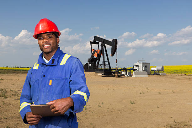 Oil Worker and Clipboard A smiling oil worker and clipboard in front of a pumpjack. oil pump oil industry alberta equipment stock pictures, royalty-free photos & images