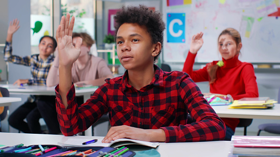 Multiethnic teen students raise hands to answer teacher question.
