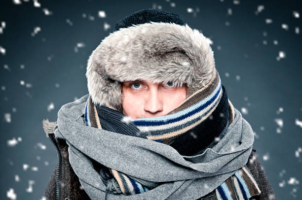 Man tightly bundled up in winter clothes, shawl, fur cap Close-up of handsome man tightly wrapped in winter clothes: shawl, cap. He has two scarves, thick warm fur cap. It is snowing, studio shot. bundle stock pictures, royalty-free photos & images