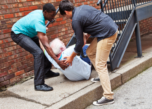 A senior white-haired man has fallen down the stairs and two young men help him up
