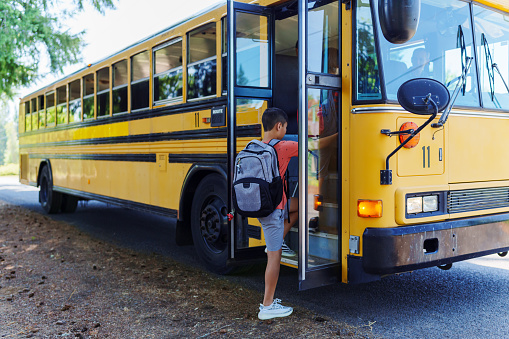 An Eurasian tween boy climbs onto the school bus which has stopped to pick him up at the school bus stop in his neighborhood.