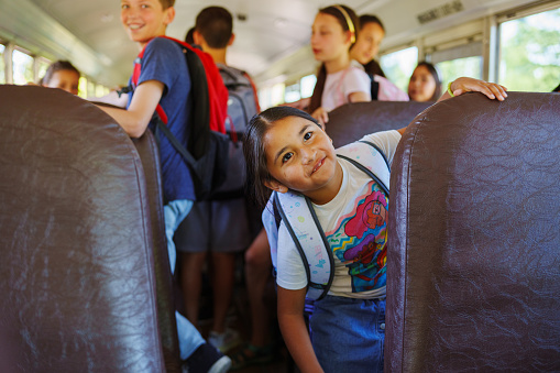 A cute young girl of Native American descent smiles while on a school bus full of elementary age students.