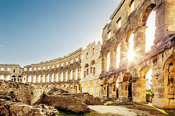 Roman Amphitheater in Pula Croatia. Built during 1st century AD, the amphitheater is the sixth largest in the world and has well preserved outer walls. Interior view with sun shining through arches into the roman colosseum. City of Pula, Croatia.