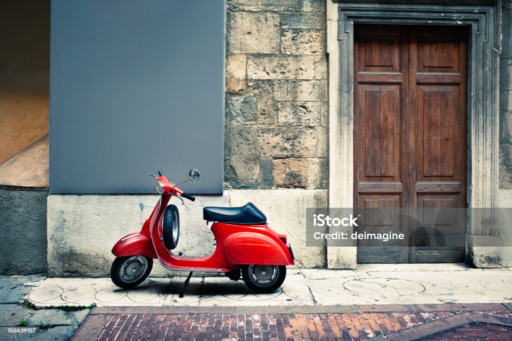 Italian vintage red scooter in front of a house A vintage red Italian scooter stands on a sidewalk beside an old-fashioned wooden door.  The wall and sidewalk are clearly old and are patched with various materials including stone and brick.  The scooter is clean and shiny looking, with a glossy black seat. Moped Stock Photo