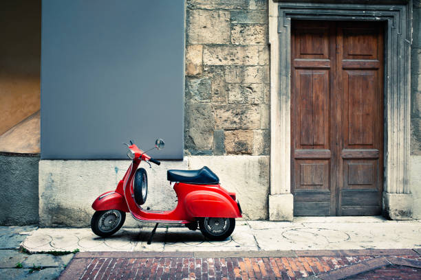 Italian vintage red scooter in front of a house A vintage red Italian scooter stands on a sidewalk beside an old-fashioned wooden door.  The wall and sidewalk are clearly old and are patched with various materials including stone and brick.  The scooter is clean and shiny looking, with a glossy black seat. moped stock pictures, royalty-free photos & images