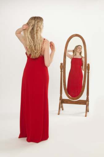 A slim, young blond woman dressed in a long red dress primping in front of a oval dressing mirror isolated on a seamless white background.http://www.garyalvis.com/images/familyLife.jpg