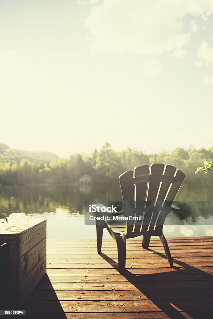 Chalet Style Adirondack chair on a jetty in front of a quiet lake at sunset. Visible lens flares. Lake Stock Photo