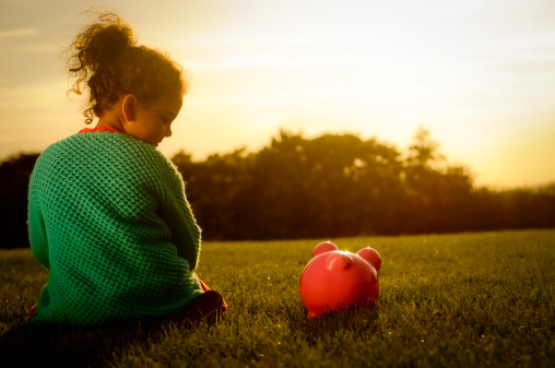 Royalty free stock photo of 6 years old girl sitting next to her piggy bank, looking at the sunset.