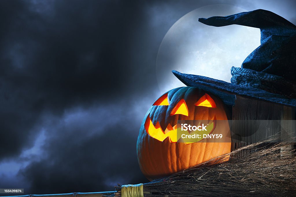 Halloween A pumpkin and a witch's hat and broom in front of a spooky full moon. Witch's Hat Stock Photo