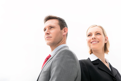 Low angle view of a beautiful businesswoman with male business partner over white background. They both look away and smile. She is a young blond hair woman. He is an ambitious young man. Waist up cropped photo. Horizontal frame with copy space.