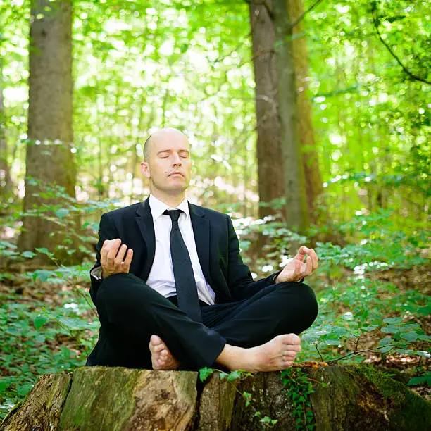 Businessman in yoga pose meditating in forest.