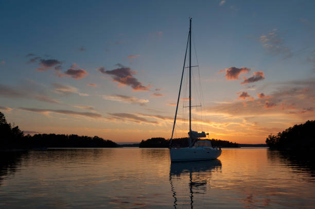Three people cruise across a tranquil lake in a small motorboat as the sun sets, creating a warm orange glow and reflections on the water's surface.