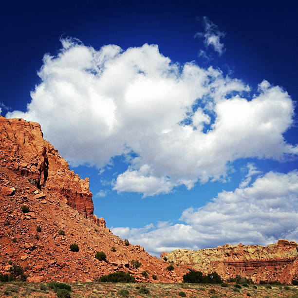 landscape desert badlands sky puffy white clouds floating in a blue sky contrast orange and red desert badlands below.  such beautiful nature scenery can be found in abiquiu, new mexico, the area popularized by the paintings of georgia o'keefe.  square composition. sonoran desert desert badlands mesa stock pictures, royalty-free photos & images