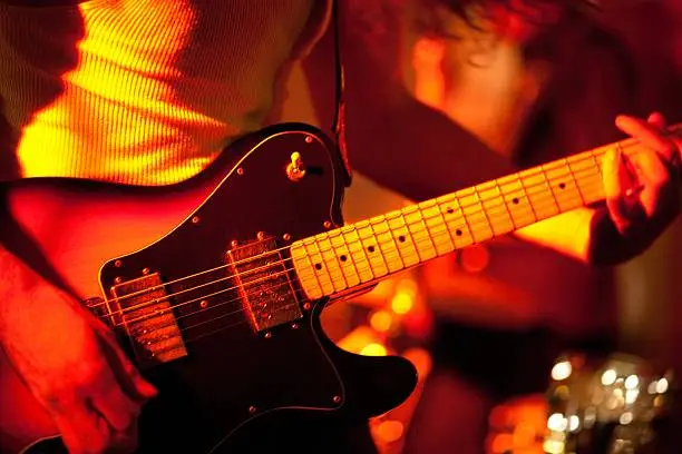 Unrecognizable musician playing an electric guitar on stage, orange, red backlight , high iso shot, shallow depth of field!, taken with prime lens and full format camera