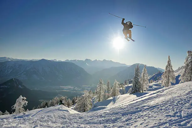 A professional freestyle skier performing a triple spin in back country against the sun. 
